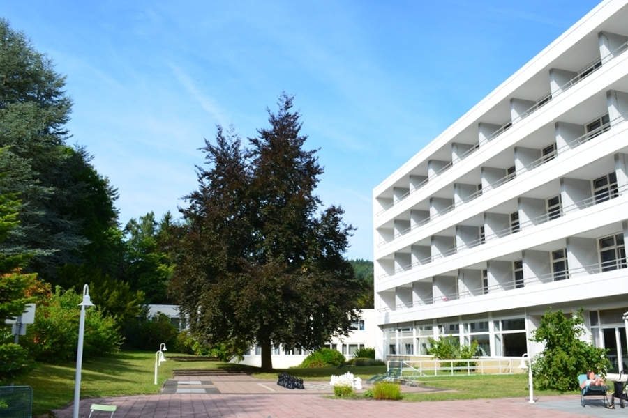 Rückansicht des Klinikgebäudes der Montanus-Klinik Bad Schwalbach mit den Balkonen der Patientenzimmer, dem angrenzenden Garten und einem Outdoor-Schachbrett.