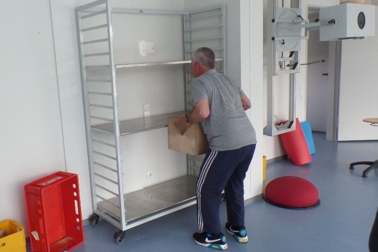 Ein Mann hebt eine Kiste rückengrecht auf ein Regal. Ein Mann hebt eine Kiste rückengrecht auf ein Regal.